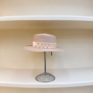 Detalle de sombrero de paja rosa con cinta de pedrería sobre un soporte de exhibición
