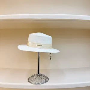 Detalle de sombrero de sol blanco con cinta crema y placa de logo dorada en un soporte