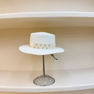 Detalle de sombrero de paja blanco con cinta de diamantes en soporte metálico
