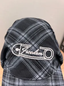 Detail of checkered newsboy cap showing white Freedom embroidery and safety pin design
