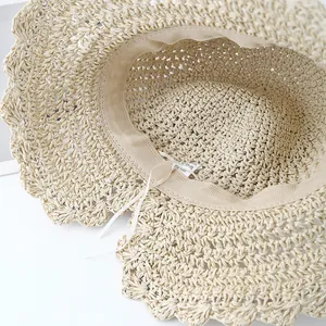 Close-up of beige paper straw sun hat with wavy brim, inner sweatband and adjustable drawstring