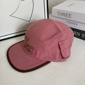 Close-up of pink camp cap with side pocket detail and green WEST COAST print