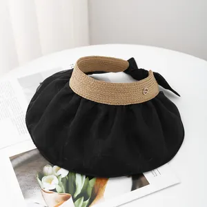 Detail view of khaki straw sun visor with black wide brim, ribbon bow and metal plaque