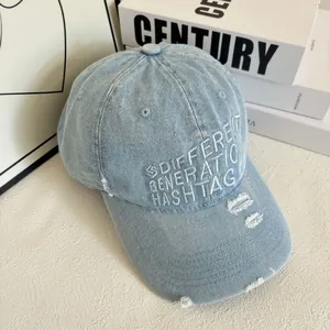 Détail d'une casquette en denim bleu clair avec broderie blanche et bords effilochés