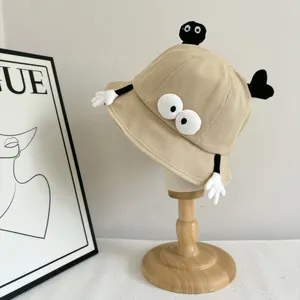 Close-up of beige bucket hat with 3D cartoon plush eyes and funny soot sprite ornaments