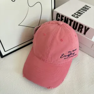 Detailed macro view of distressed pink cotton baseball cap with embroidered text and tag