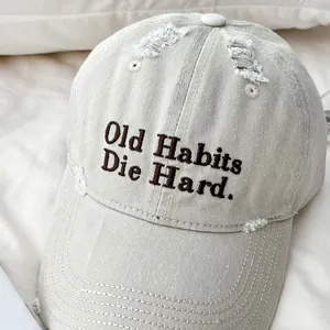 Detalle del bordado 'Old Habits Die Hard' en una gorra de béisbol beige de estilo retro