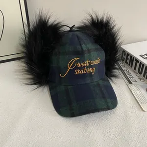 Detail of plaid baseball cap with black faux fur pom-poms and West Coast Skating embroidery
