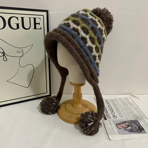 Close-up of Fair Isle knit winter hat with ear flaps and fluffy brown pompoms on wooden stand