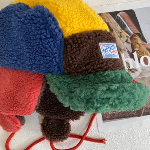 Detalle del gorro de aviador de lana de cordero multicolor con textura suave y lazos rojos