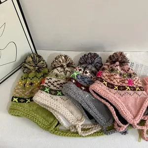 Knit trapper hat with pompom and embroidery in four colors on a white background