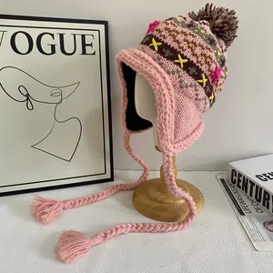 Detailed view of pink knitted earflap hat with colorful geometric patterns and tassels