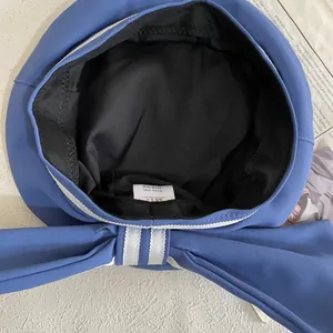 Detail of blue beret featuring a large bow and internal sailor-style striped ribbon trim