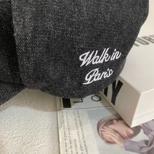 Close-up of black denim baseball cap featuring white Walk in Paris embroidery detail