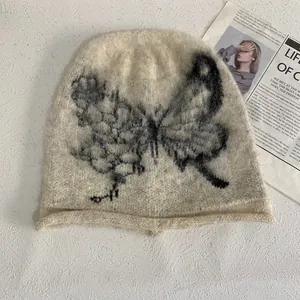 Close-up of cream knit beanie featuring black butterfly jacquard and fuzzy mohair texture