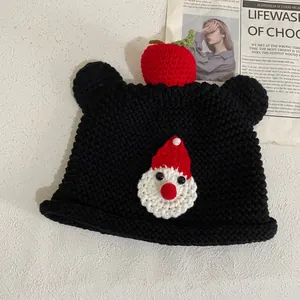 Detail der handgestrickten Bärenmütze mit Weihnachtsmann-Häkelarbeit und Apfel