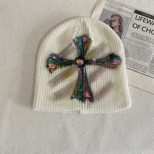 Detail view of cream knitted beanie featuring a colorful graffiti spray-painted cross