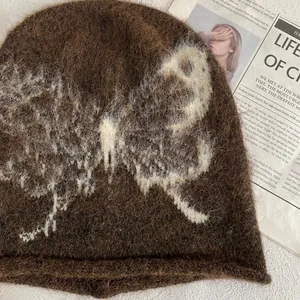 Close-up of brown mohair knit beanie featuring white butterfly pattern and fuzzy texture