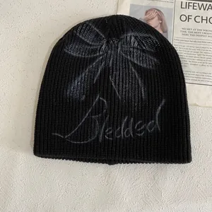 Detail of black ribbed knit beanie featuring a grey bow graphic and Blessed text