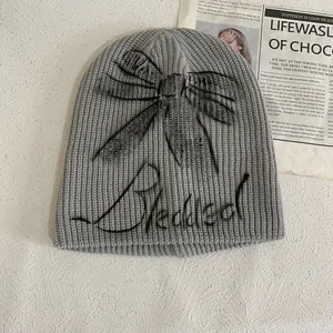 Detail of grey knitted beanie with black graffiti bow and Bleakleaf script embroidery
