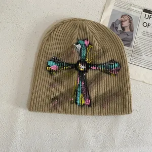 Detailed shot of khaki knitted beanie featuring a colorful graffiti cross design