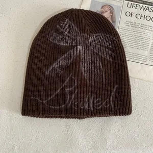Detail view of brown knit beanie featuring light gray butterfly graffiti and script text