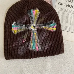 Detailed close-up of brown knit beanie with colorful cross graffiti on white surface