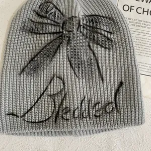 Detail of light grey knit beanie featuring a black bow pattern and embroidered text