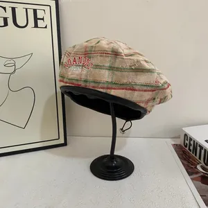 Detailed view of plaid beret hat showing texture, leather trim and embroidered logo