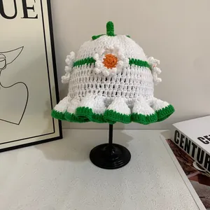 Close-up of handmade white knit bucket hat with green wavy edge and daisy flowers