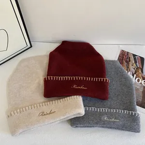 Detalle de gorros de punto en beige, burdeos y gris con elegante bordado Rainbow