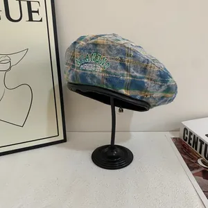 Detailed close-up of retro plaid beret with embroidered letters and leather piping edge