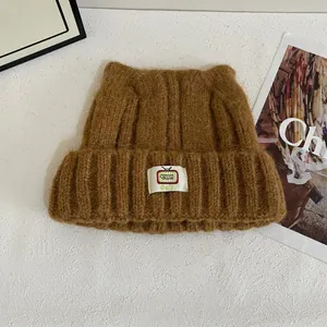 Primo piano di un cappello di maglia marrone con orecchie di gatto e toppa con logo bianco