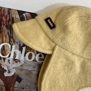 Dettaglio del cappello da aviatore in pile giallo con texture morbida ed etichetta logo