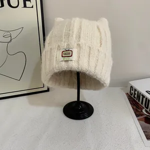 Dettaglio del berretto in maglia bianco crema con orecchie di gatto e toppa logo TV