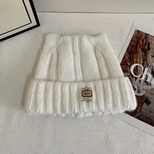 Dettaglio del cappello in maglia bianca con orecchie da gatto e toppa TV