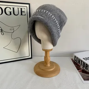 Detalle de gorro de punto gris oscuro con bordado de mariposa y costuras blancas hechas a mano