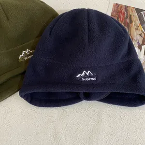Detalle de gorros de forro polar azul marino y verde oliva con bordado de montaña