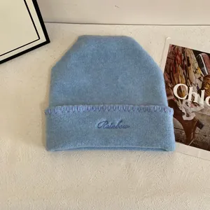 Detalle de gorro de punto azul claro con costuras púrpuras y bordado Rainbow en el dobladillo