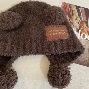 Dettaglio del cappello di peluche marrone con orecchie da orso, ricamo e morbida trama in pile