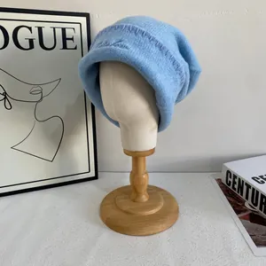 Detalle de gorro de punto azul claro con costuras decorativas moradas sobre soporte