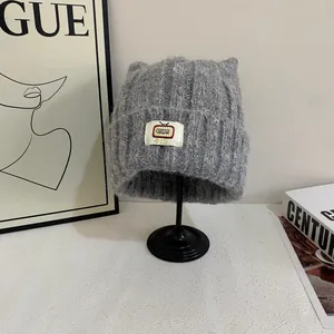 Dettaglio di un cappello a maglia grigio con orecchie da gatto e targhetta decorativa