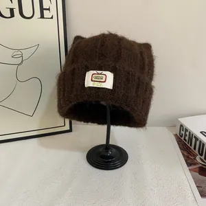 Dettaglio del berretto in maglia marrone con orecchie di gatto e toppa TV su supporto