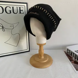 Detalle de gorro de punto negro con costura beige y bordado de arco iris