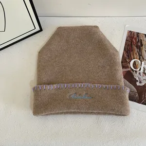 Detalle de gorro de punto marrón con borde morado y bordado Rainbow en azul claro