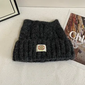 Dettaglio di un cappello in maglia grigio scuro con patch TV su superficie ruvida