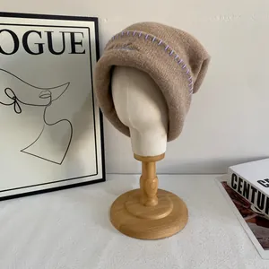 Detalle de gorro de punto marrón con bordado azul claro y ribete morado cosido a mano