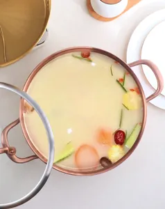 Vertical top view of rose gold dual-handle hot pot with a clear glass lid and soup