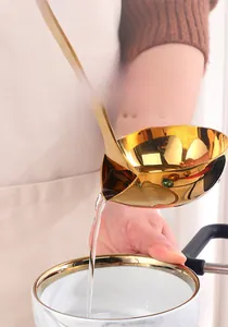 Close-up of golden stainless steel oil separator spoon pouring clear soup in a kitchen