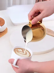 Detailed close-up of golden stainless steel milk pitcher pouring latte art into a cup